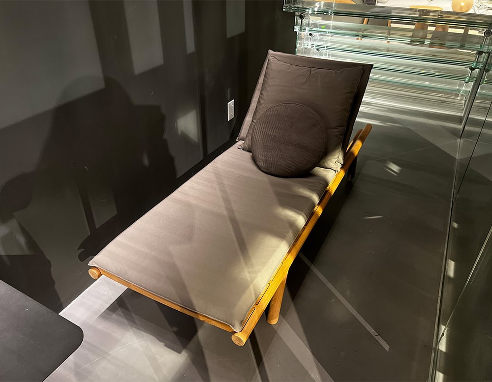 A sleek and modern Rod Orson Sun Lounger featuring a wooden frame with plush dark cushions set in a stylish contemporary space