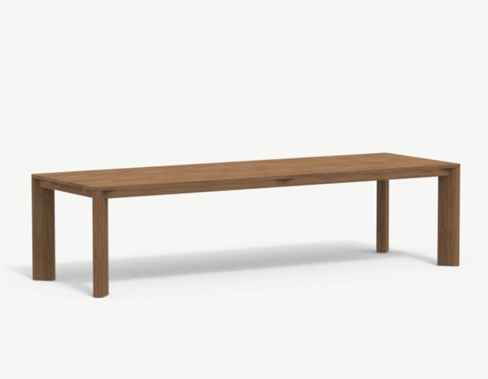 A long outdoor dining table in natural teak with clean lines, square legs, and a minimalist silhouette designed for versatility and durability.