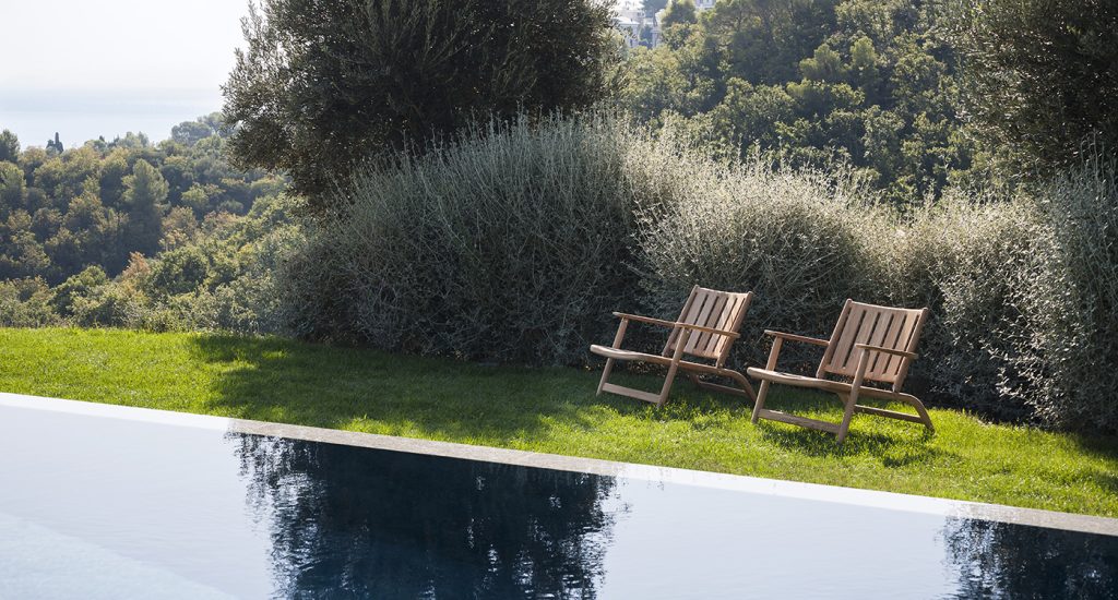 Two Levante Seven Lounge Chair in front of a pool with bushes in the background