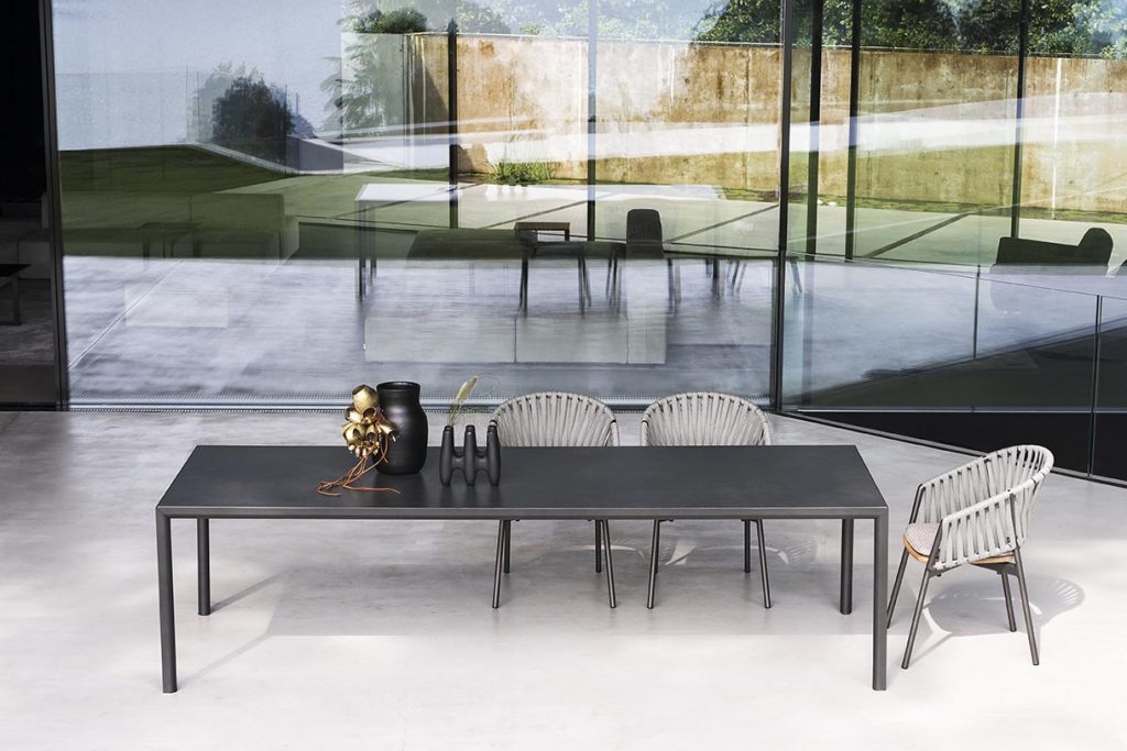 Plen Air Five Table with chairs behind it and a large long glass in the background