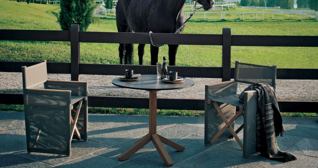 Root Three Table between two armchairs outside with a wooden farm fence behind and a horse behind the fence