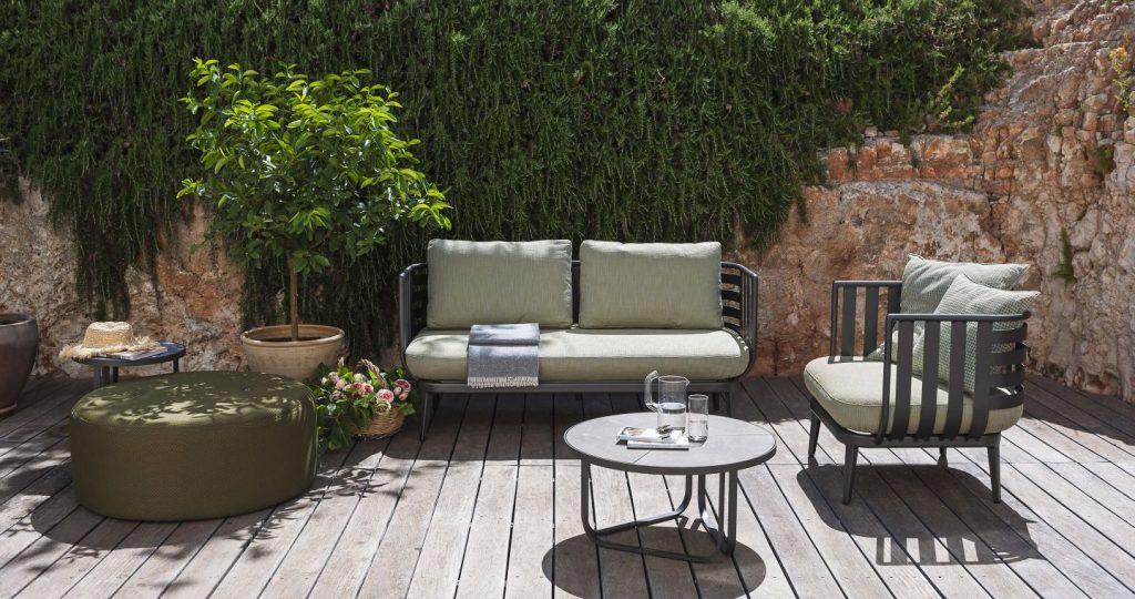 Thea Two Sofa with a coffee table in front and a hedge in the back on a patio