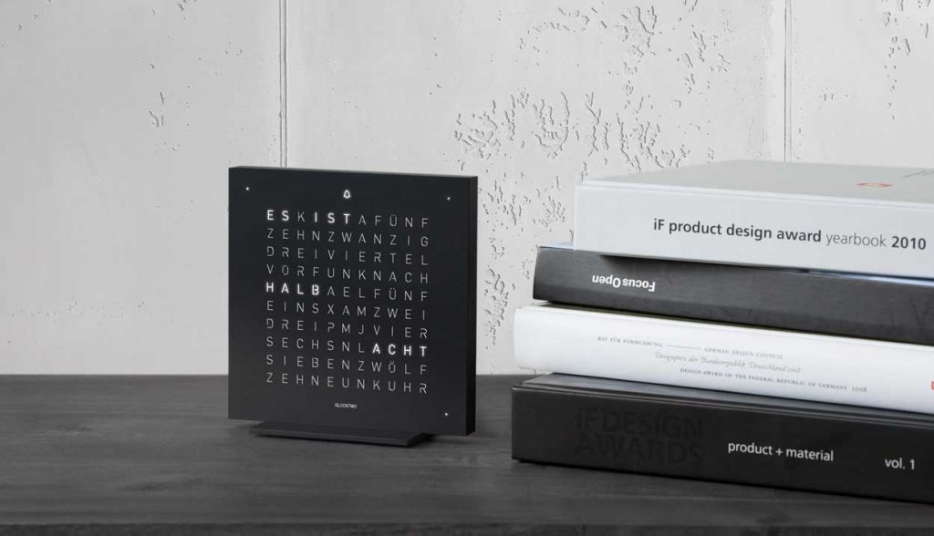 QLOCKTWO Touch in black on a black desk with books to the right stacked up