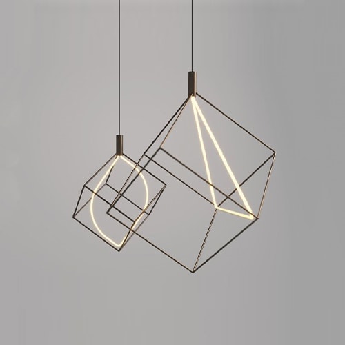 Pair Spectrum lights hanging from the ceiling. One has a triangular bulb in the middle of the cube frame and the other has an oval bulb in the middle of the cube frame in front of a white background