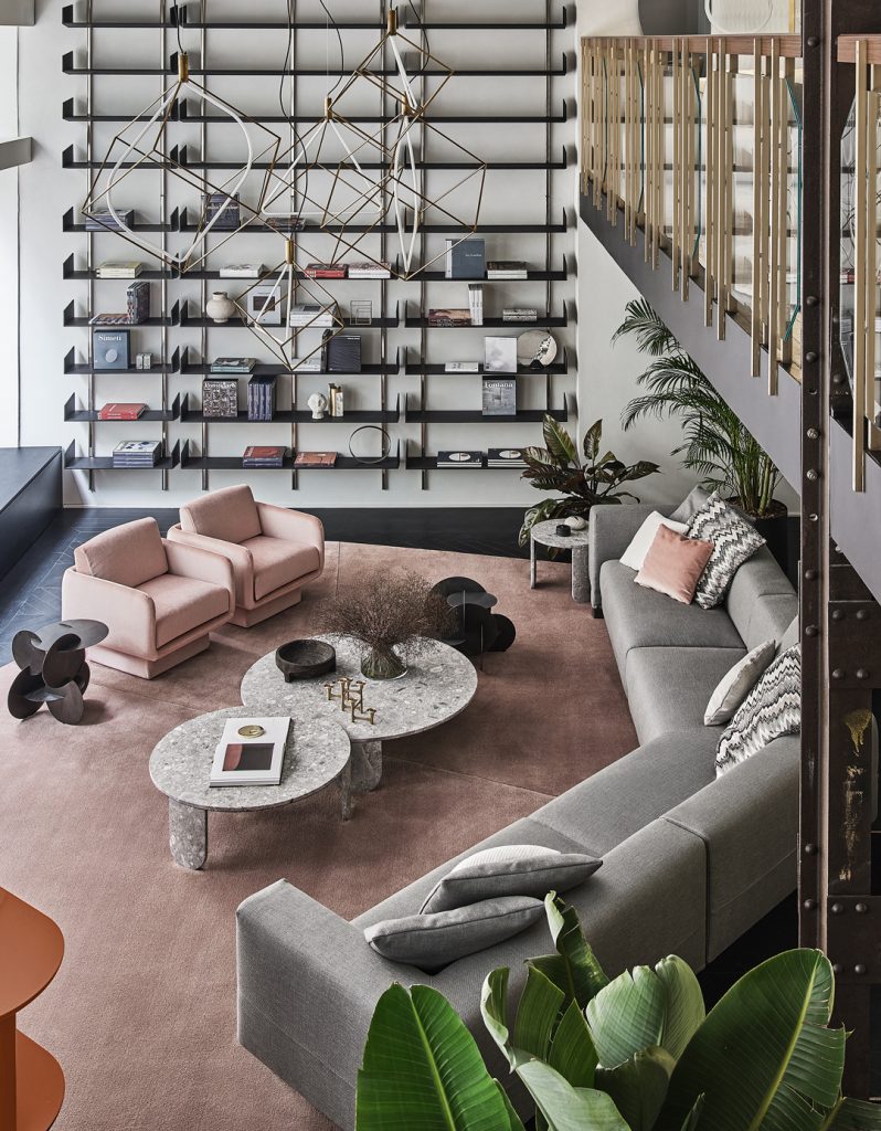 Elissa Sectional with multi colored pillows on top, two round coffee tables in front, a book shelf to the right side in front of a grey wall