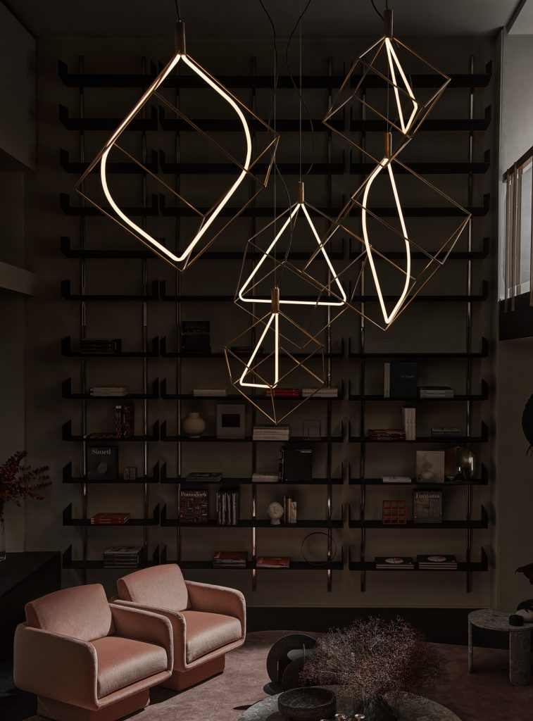 Quad Spectrum lights hanging from the ceiling. Two have a triangular bulb in the middle of the cube frame and the other two have an oval bulb in the middle of the cube frame with a dark brick wall in the background and a sofa below it