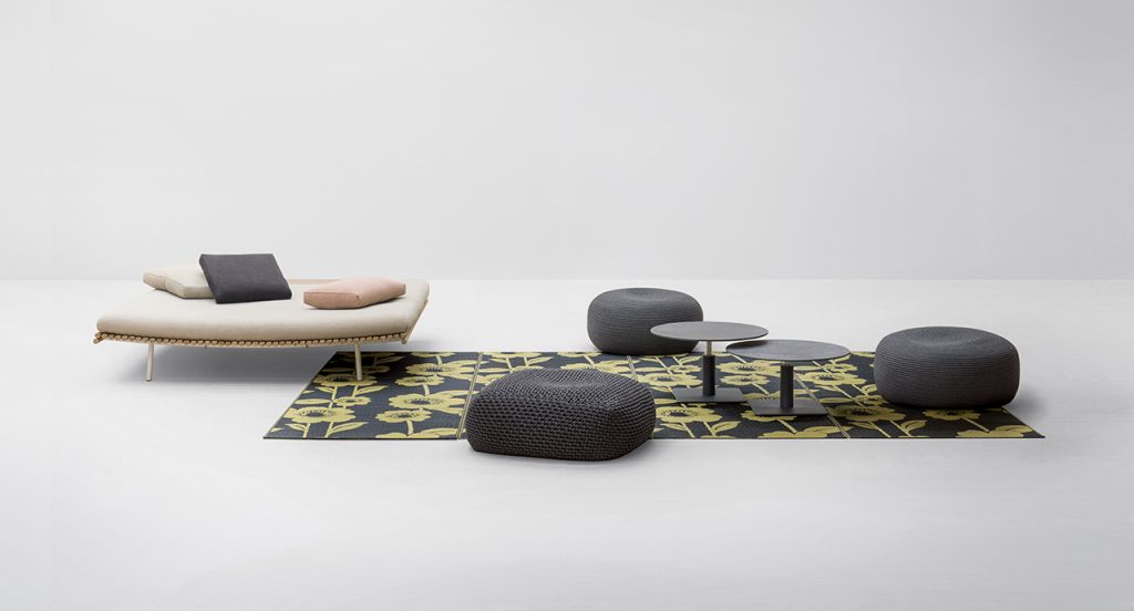 Shibui Platform behind a green rug with a table on top of the rug and a pair of small black chairs in front of a white background
