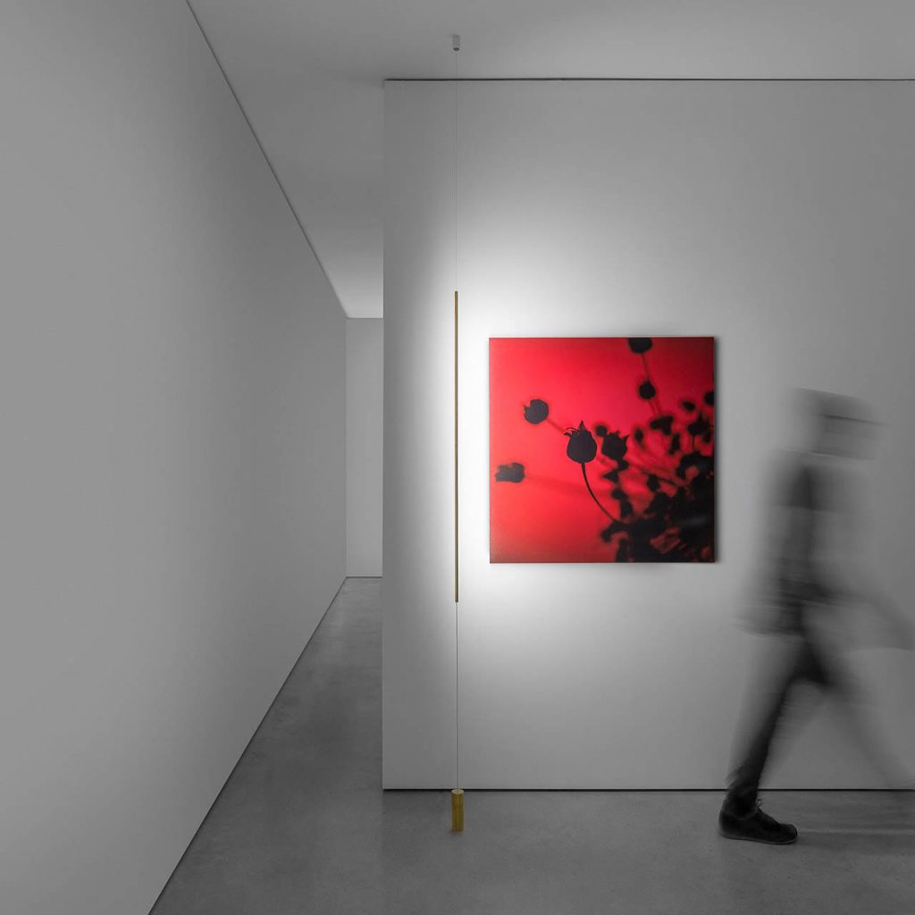 Masai light shining on a red painting with a person walking on the right side of the painting