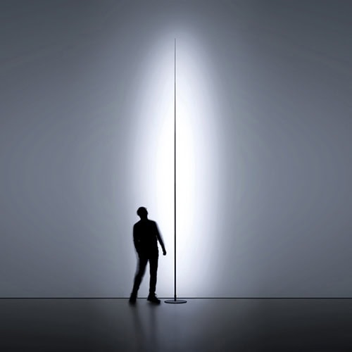 Origine light shining against a white wall with a person standing behind the light looking upwards