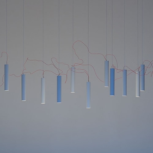 Simbiosi chandelier hanging in front of a grey wall
