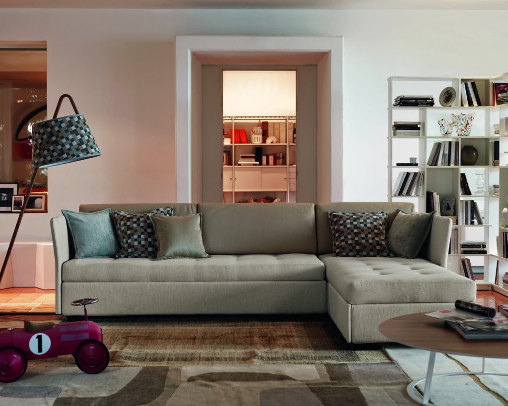 Figi in a grey color on top of a multicolored rug and a white wall in the background with an open hallway
