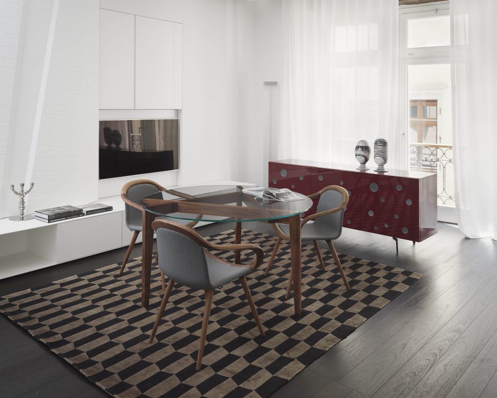 Autoreggente with a circular glass top surrounded by chairs on top of a checkered brown rug with a white wall background