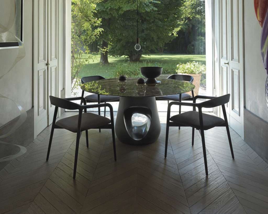Barbara surrounded by black chairs on top of a dark wood floor and windows behind the table