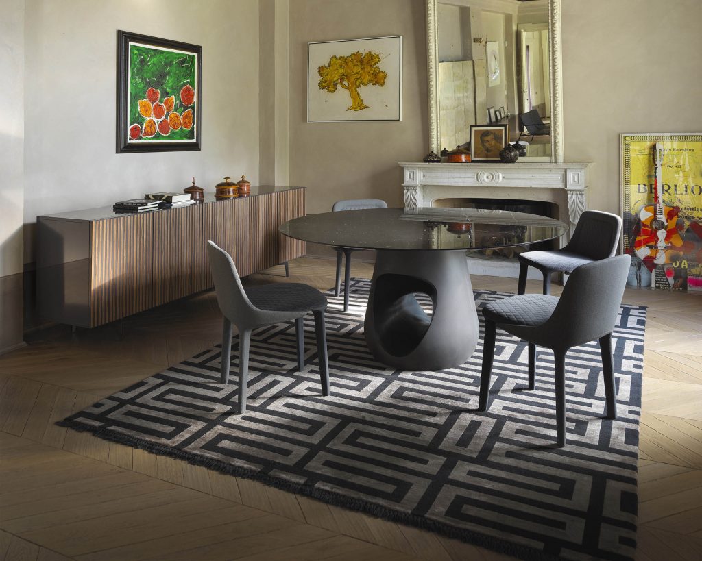 Barbara surrounded by black chairs on top of a maze patterned rug