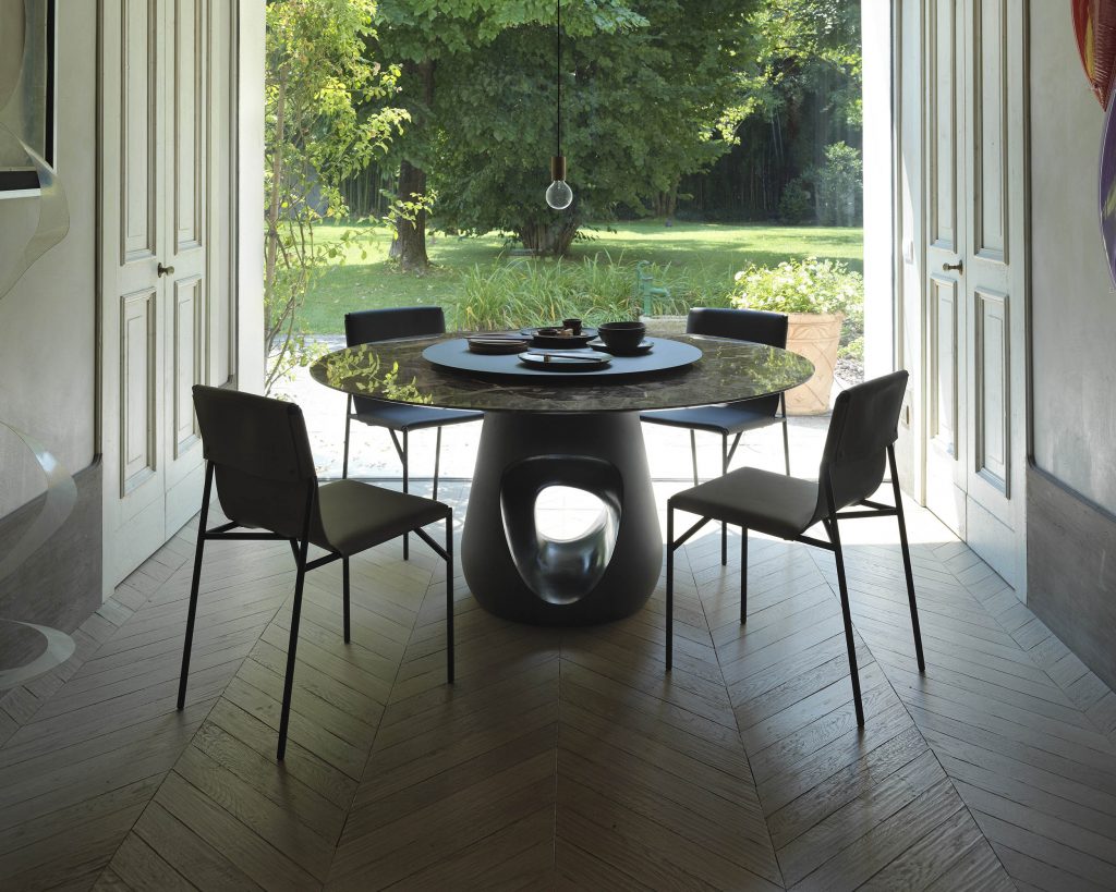 Barbara surrounded by black chairs on top of a dark wood floor and windows behind the table