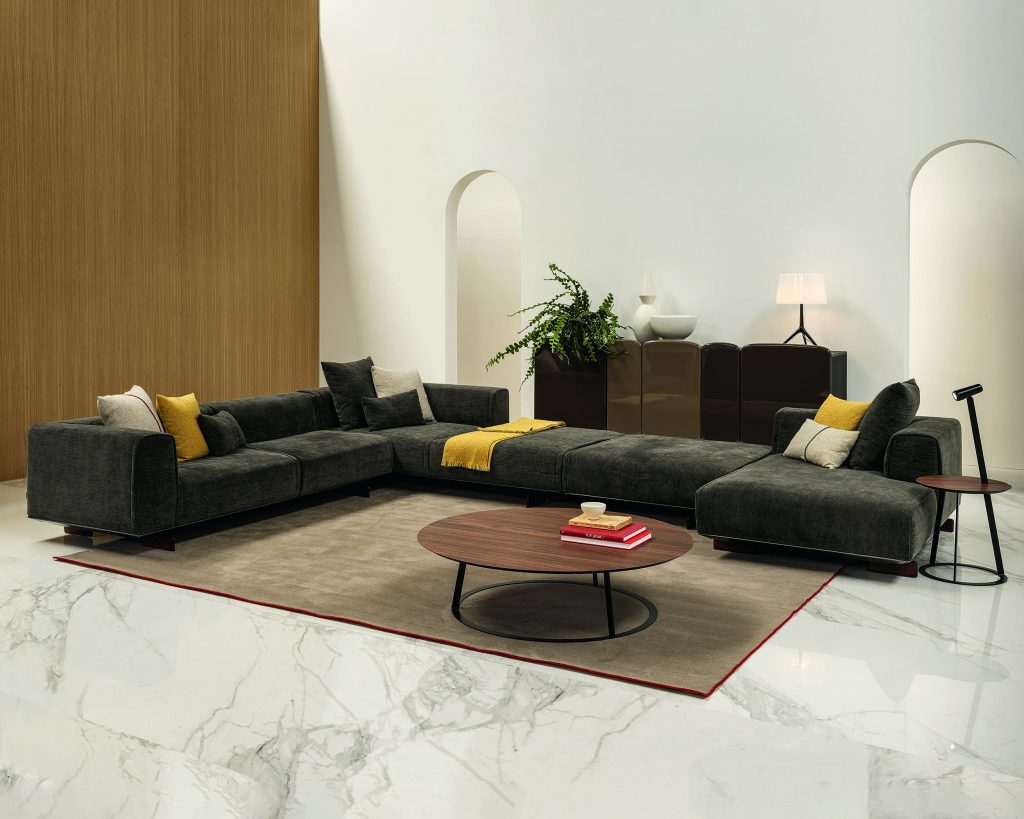 Dark-colored Coleman in a large L-shaped configuration with a brown coffee table in the middle and white walls surrounding the sofa
