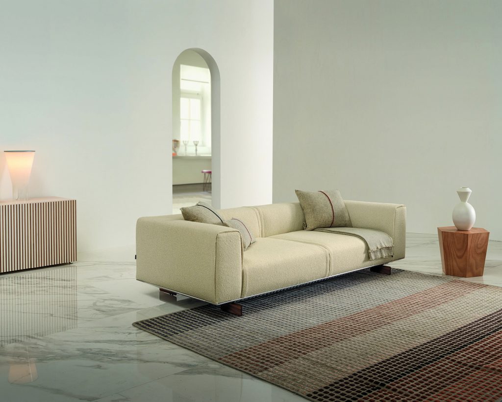 Angled view of cream colored Coleman on a multicolored rug and white walls surrounding the sofa