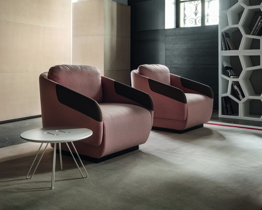 A pair of pink Worn chairs side by side with a small gap between them with a cream colored wall behind them