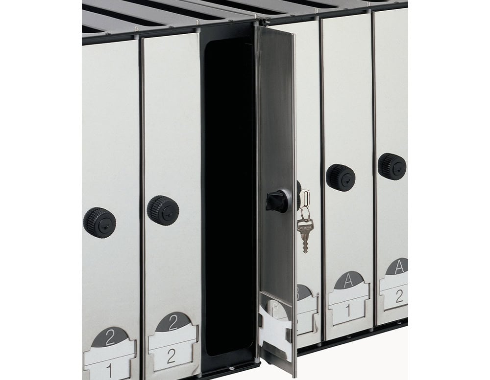 A close-up of stainless steel mailbox modules, one door open to reveal the interior, highlighting the locking system and numbered label slots.