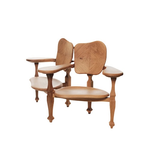 The BD Batllo Bench in light oak wood features two organically contoured seats with curved backrests and integrated armrests, emphasizing artisanal detailing and sculptural elegance.