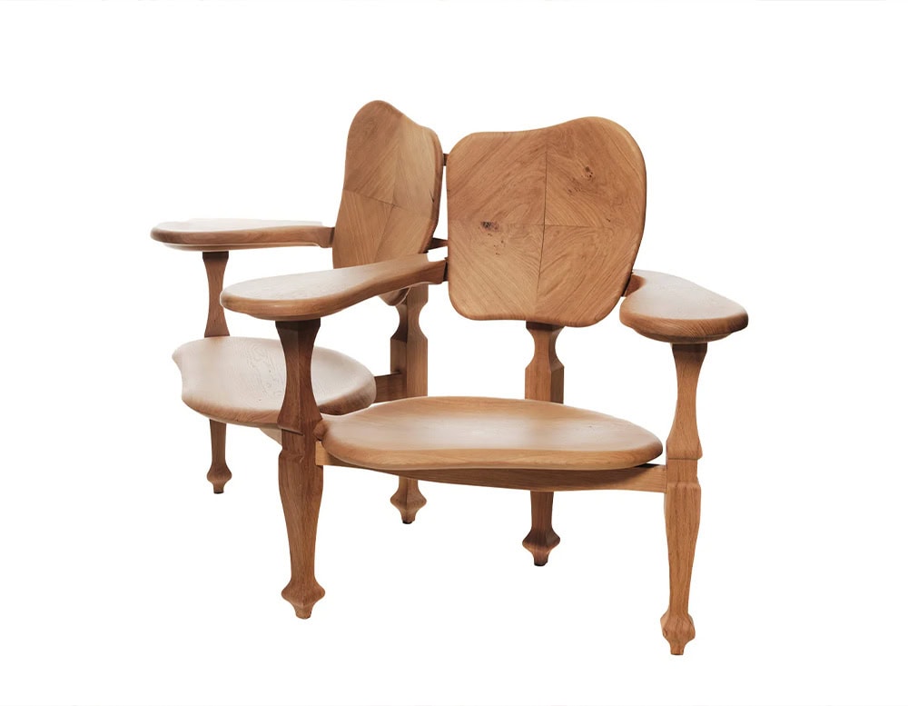 The two-seater BD Batllo Bench, crafted in light oak wood, features organically contoured seats and backrests with visible grain patterns, paired with sculptural legs and flowing armrests for a fluid, handcrafted look.
