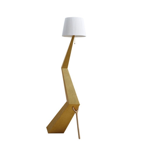 The lamp features a sculptural gold-toned angular base, contrasted with a slender wooden support and topped with a simple white fabric shade. Its dynamic shape evokes a sense of balance and architectural elegance.