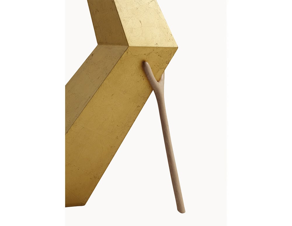 This close-up highlights the lamp’s gold-toned angular structure and its distinct support element resembling a natural wooden branch, adding an organic contrast to the geometric form.