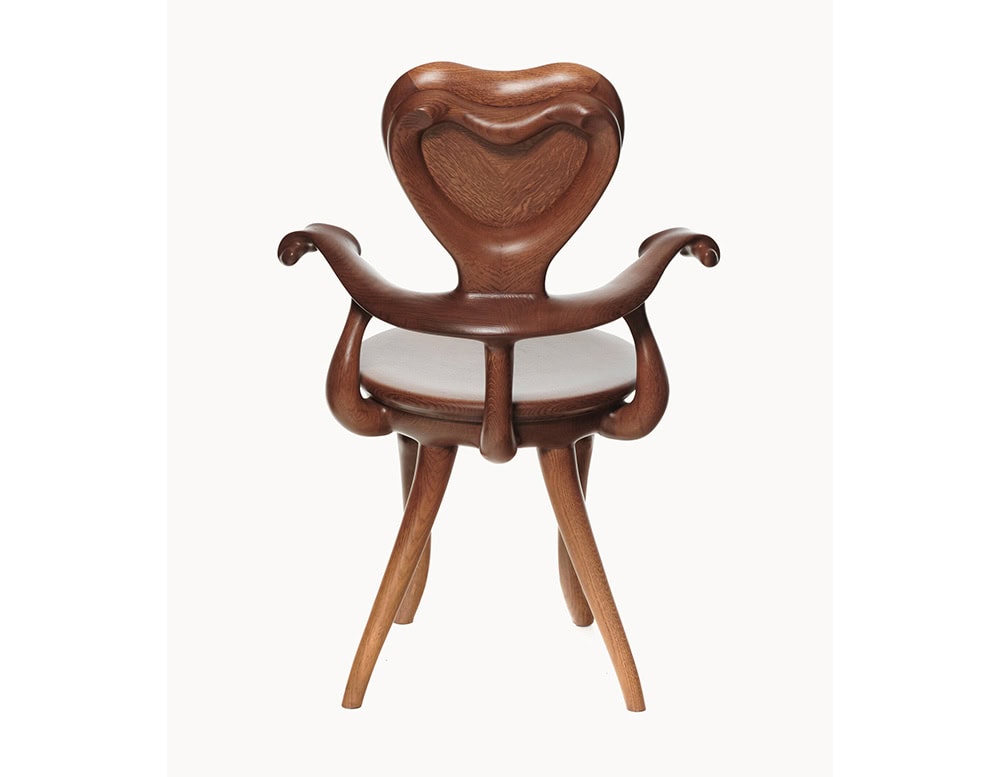 The BD Calvet Armchair is presented from the back, highlighting its sculptural backrest, fluid armrests, and four elegantly curved legs. The chair features a warm, medium-brown wood finish with visible grain texture.