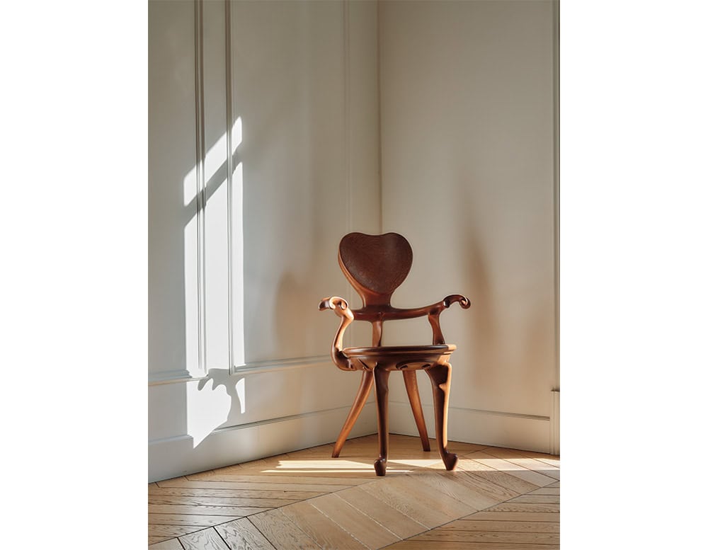 The BD Calvet Armchair is placed in a bright corner where natural light highlights its sculptural curves. The heart-shaped backrest, flowing armrests, and refined craftsmanship create a striking silhouette against the paneled walls.