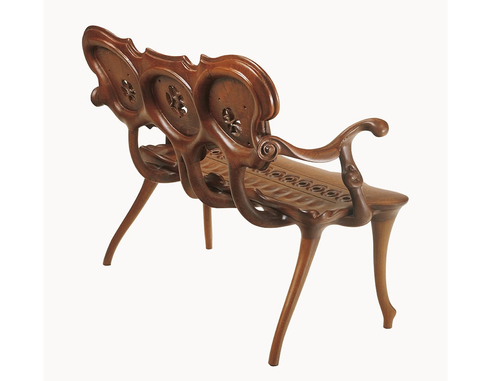 The BD Calvet Bench is captured from the back, revealing its sculptural frame and sinuous lines. The hand-carved details and fluid design of the bench highlight the organic forms characteristic of its artistry.