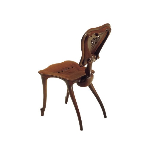 The BD Calvet Chair is shown from an angled perspective, revealing its flowing wooden curves, sculptural backrest, and perforated seat. Its distinctive form merges functional design with artistic elegance in a seamless composition.