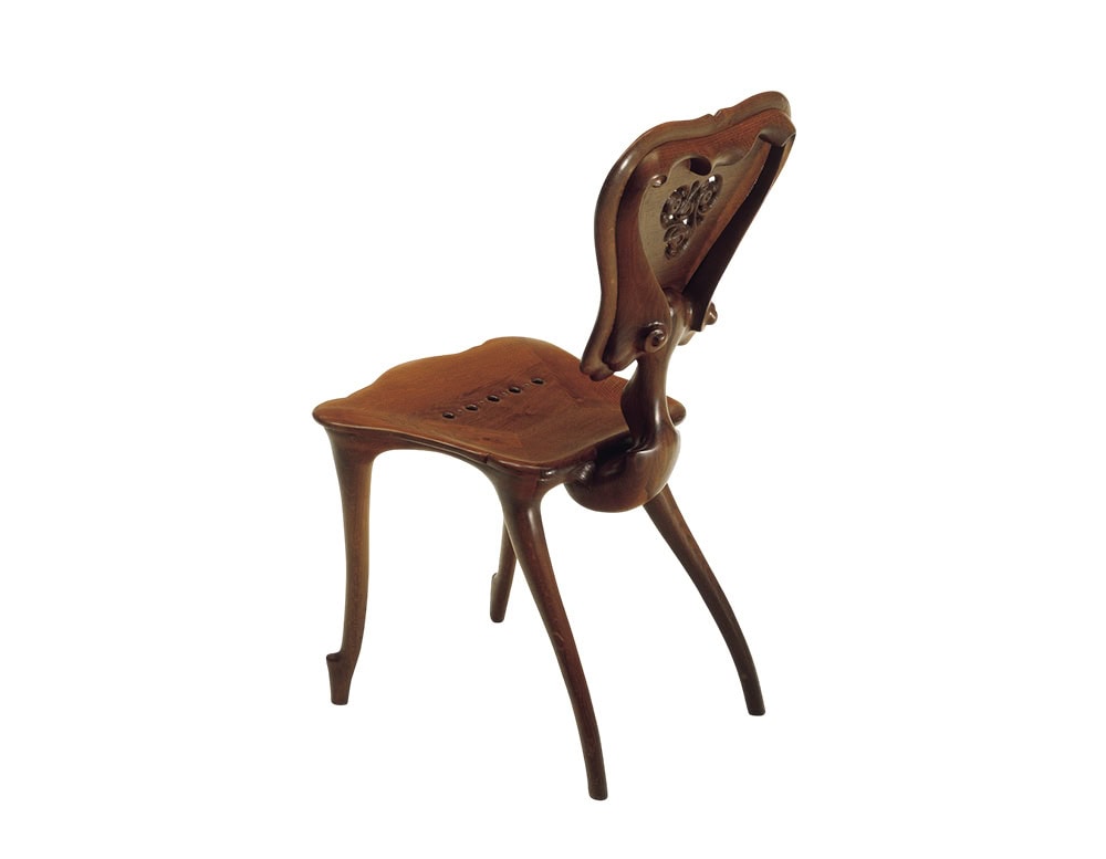 The BD Calvet Chair reveals its sinuous structure from the back, with curved legs and a seat carved for comfort. The wooden backrest features an ornamental floral carving, highlighting craftsmanship and elegance.
