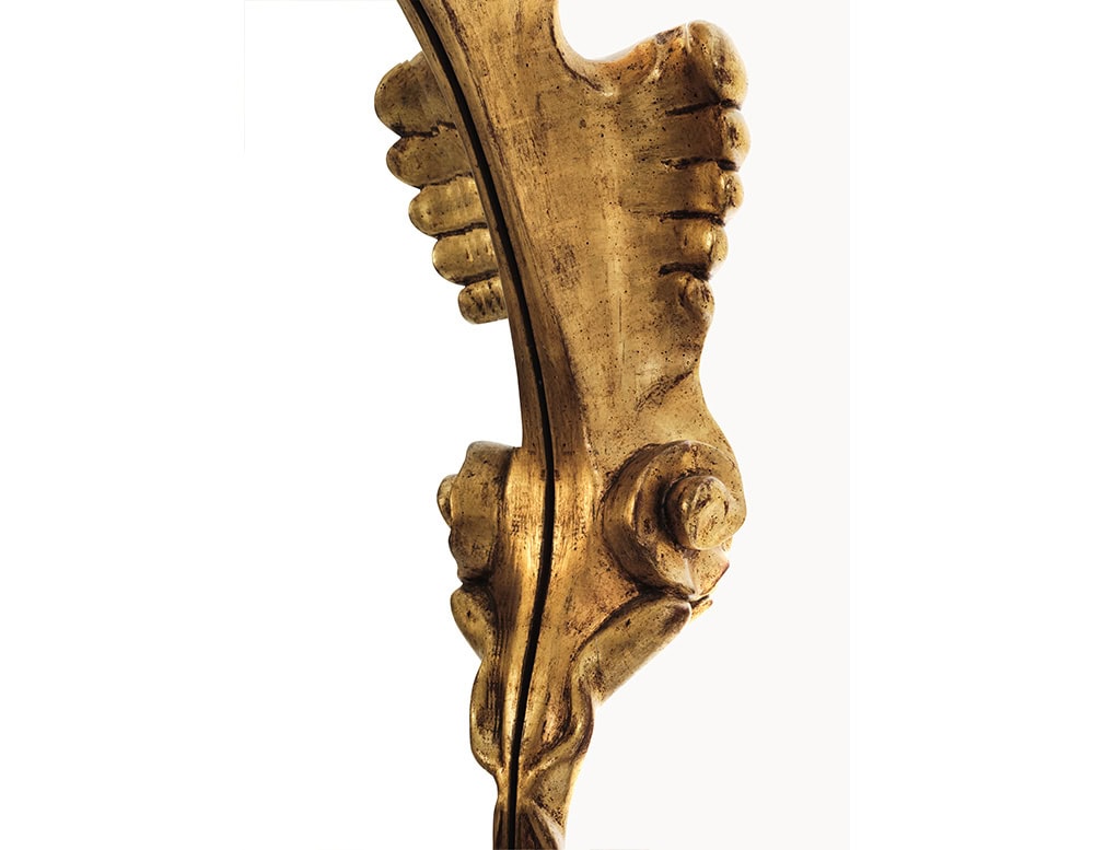 A close-up view reveals the BD Calvet Mirror's hand-carved wooden frame with intricate curves and a rich gold leaf finish, highlighting the craftsmanship and texture of this luxurious decorative piece.
