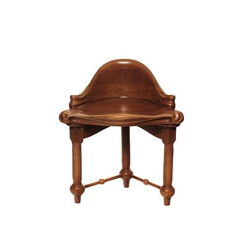 This view emphasizes the detailed craftsmanship of the Calvet Stool, showcasing its curved seat, carved edges, and characteristic triangular leg arrangement.