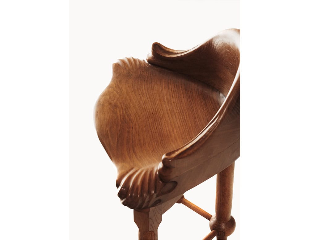 An angled perspective reveals the Calvet Stool’s sculptural curves, emphasizing the flowing grain of the carved seat and the fluid transition from backrest to leg. The rich finish highlights the organic texture of the wood.