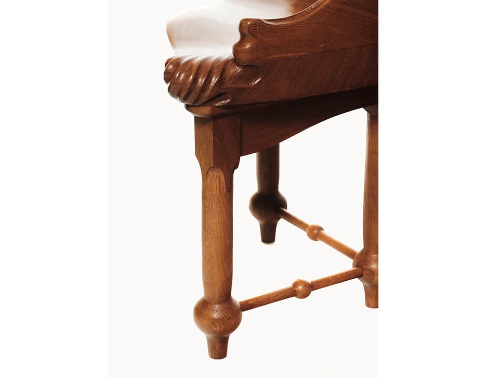A close view reveals the intricate carved edge of the Calvet Stool’s seat paired with its faceted leg design. The wood’s polished surface and the softly rounded stretcher connection reflect the craftsmanship and natural material beauty.