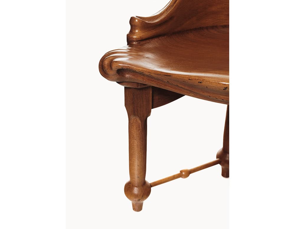 An intimate perspective captures the fluid contour of the Calvet Stool’s seat edge, emphasizing the smooth wood curves, hand-carved grooves, and the turned leg with its delicate connecting stretcher. The finish highlights the natural grain.