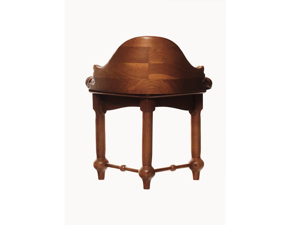 The image presents the Calvet Stool in a direct frontal perspective, highlighting its sculptural wood grain and rich finish. The curved backrest seamlessly blends into the legs, showcasing craftsmanship with flowing organic lines and carved details.