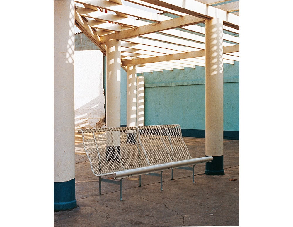 A BD Catalano bench set under a geometric pergola structure. The bench’s perforated steel mesh and subtle curves complement the industrial setting while providing practical, comfortable seating for outdoor environments.