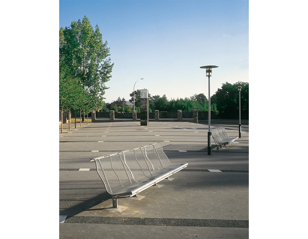 A pair of BD Catalano outdoor benches positioned in an open plaza. The benches feature a curved, perforated metal design that offers visual lightness while maintaining durability for public use.
