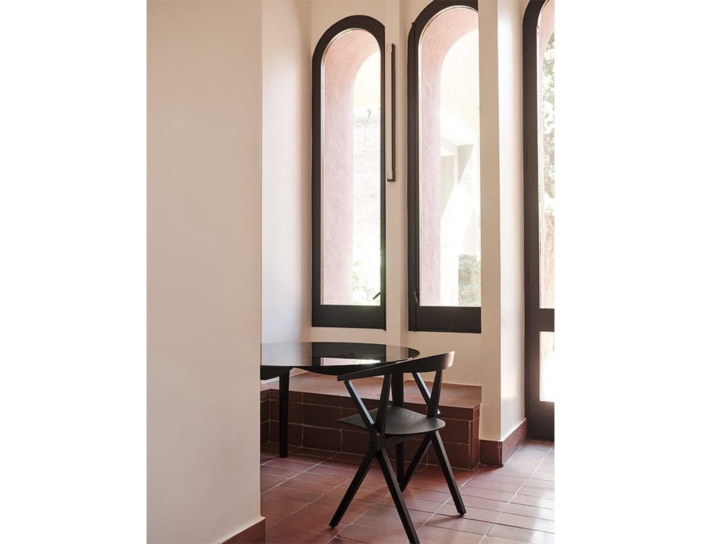 A serene corner featuring the BD Chair B in matte black, paired with a minimalist black table. The natural light from the tall arched windows enhances the contrast between the geometric furniture and the architectural details.