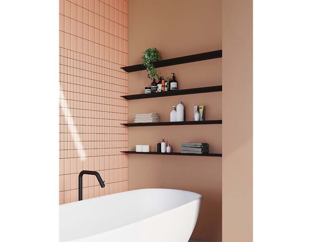 The BD Cornisa Shelf in matte black is featured in a bathroom setting with a warm terracotta wall, neatly holding towels, toiletries, and small decorative elements, offering a sleek and functional storage solution.