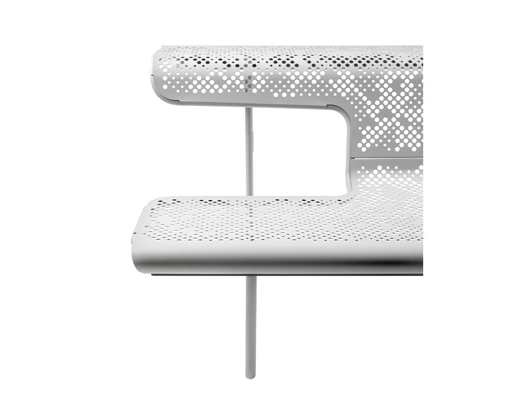 Close-up of the El Poeta bench in a light finish, highlighting its layered seat and backrest. The perforated metal surface forms a subtle pattern, while the slim vertical supports keep the structure visually light.