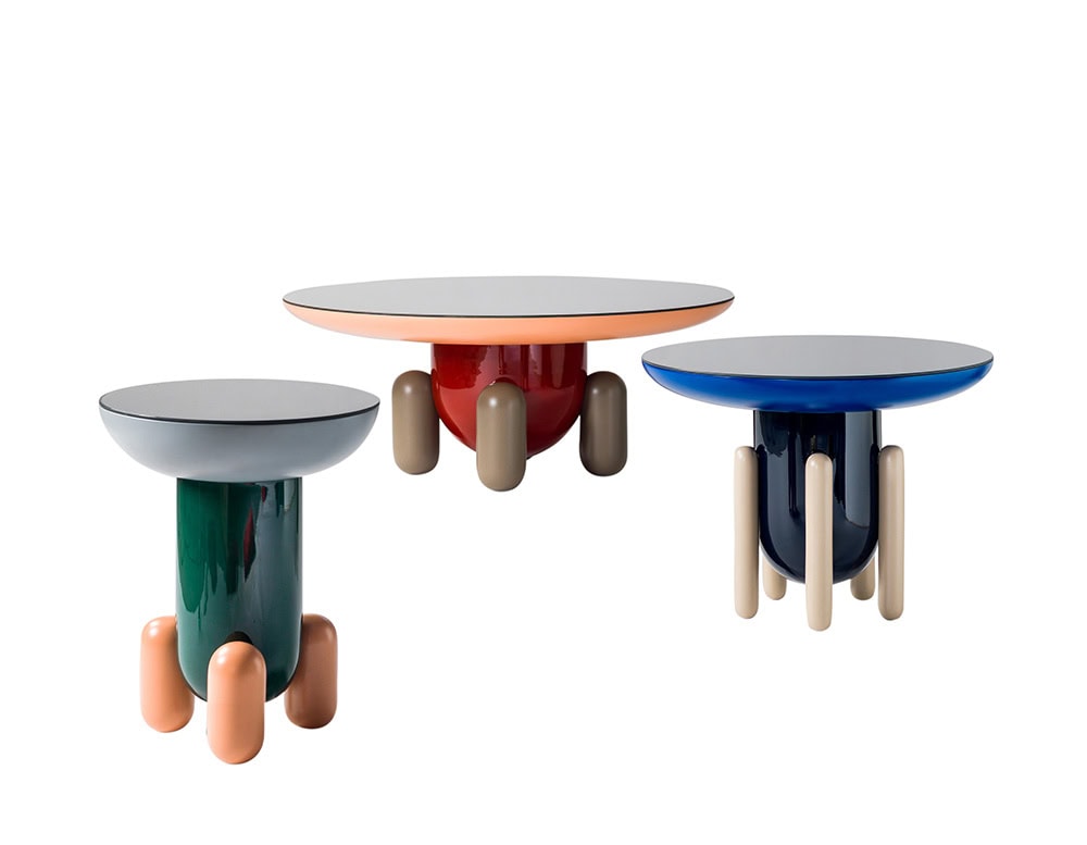 A trio of BD Explorer tables with glossy finishes and bold colors. Each piece combines a smooth lacquered top with rounded legs, contrasting playful forms and polished surfaces in green, red-orange, and deep blue.