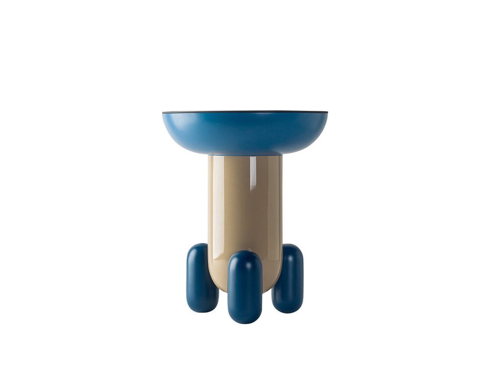 A playful side table featuring a glossy blue top and rounded navy legs. The central base is finished in a soft beige tone, creating a bold contrast with the vibrant upper and lower elements.