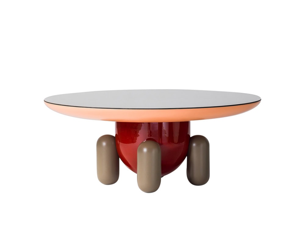 A round side table featuring a soft orange edge, glossy red base, and playful taupe legs. Its sculptural silhouette blends whimsy with modern design.
