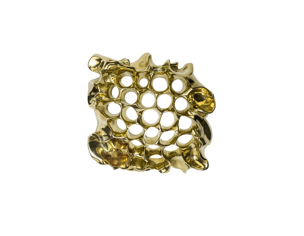 A sculptural brass piece with a fluid, organic design and perforated pattern. Its glossy finish highlights the irregular contours, creating an eye-catching wall element or decorative accent that combines artistry with functional detail.