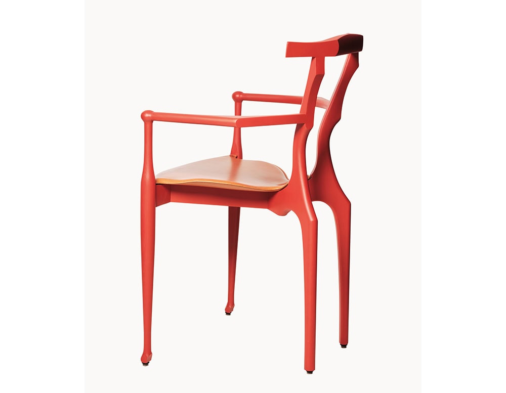 Side angle of a red BD Gaulino Chair with a tan leather seat, highlighting its refined silhouette, flowing curves, and graceful armrest design.