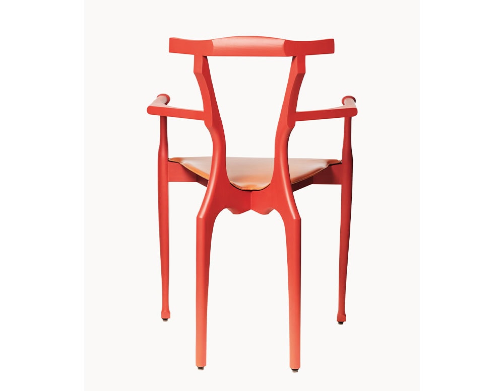 A red BD Gaulino Chair with a tan leather seat, highlighting its intricate silhouette, slender legs, and fluid backrest in a clean, minimal setting.