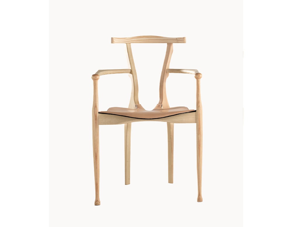 A natural ash wood BD Gaulino Chair with a tan leather seat, showcasing its sculptural backrest, refined armrests, and minimalist structure.